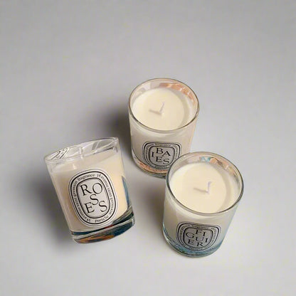 three decorative candles (figuier, roses and baies) in a white glass jar on white background