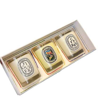 box with three decorative candles (figuier, citronnelle and cypres)  in a white glass jar on white background
